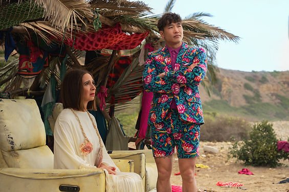 Maya Rudolph sat down on a chair and Joel Kim Booster stood up beside her with his arms crossed in 'Loot,' 