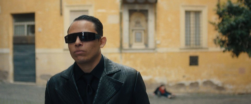 Anthony Ramos as The Assassin wearing dark sunglasses in front of a building in 'The Beauty'