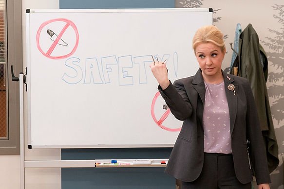 Wendi McLendon-Covey as Joyce stood in front of a white board with "Safety" written in bubble writing and blue ink, holding keys between her fist in "Mama Bear Activated."
