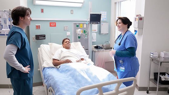 Mekki Leeper as Matt, and Allison Tolman as Alex stood by a patient's bedside in St. Denis Medical.
