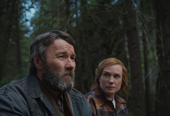 Joel Edgerton as Robert Grainier and Kerry Condon as Claire Thompson sat in a forest in Train Dreams.