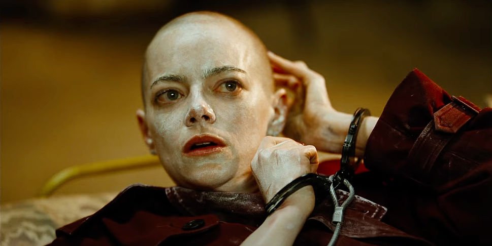 Emma Stone as Michelle Fuller with a surprised look on her face touching her bald head in 'Bugonia'