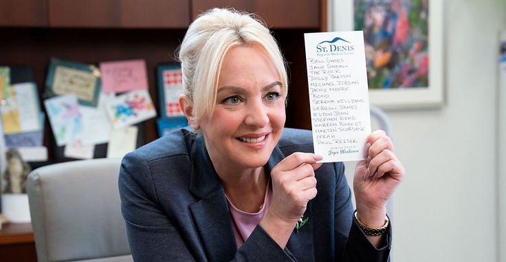 Wendi McLendon-Covey as Joyce holding a list of celebrities in her office in St. Denis Medical Season 2 Episode 6.