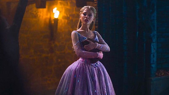 Ariana Grande as Glinda holds a book to her chest in a torchlit scene in 'Wicked: For Good'.