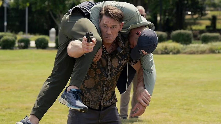 John Cena as Chris carries Brandon Stanley as Kline over his shoulders and fires a pistol in 'Peacemaker'. 