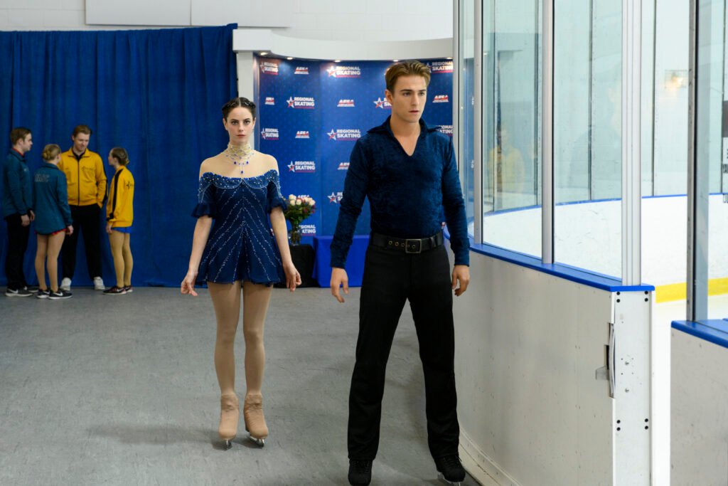 Kaya Scodelario as Kat Baker and Evan Roderick as Justin Davis in Spinning Out, wearing their competitive figure skating costumes as they prepare to perform on the ice.