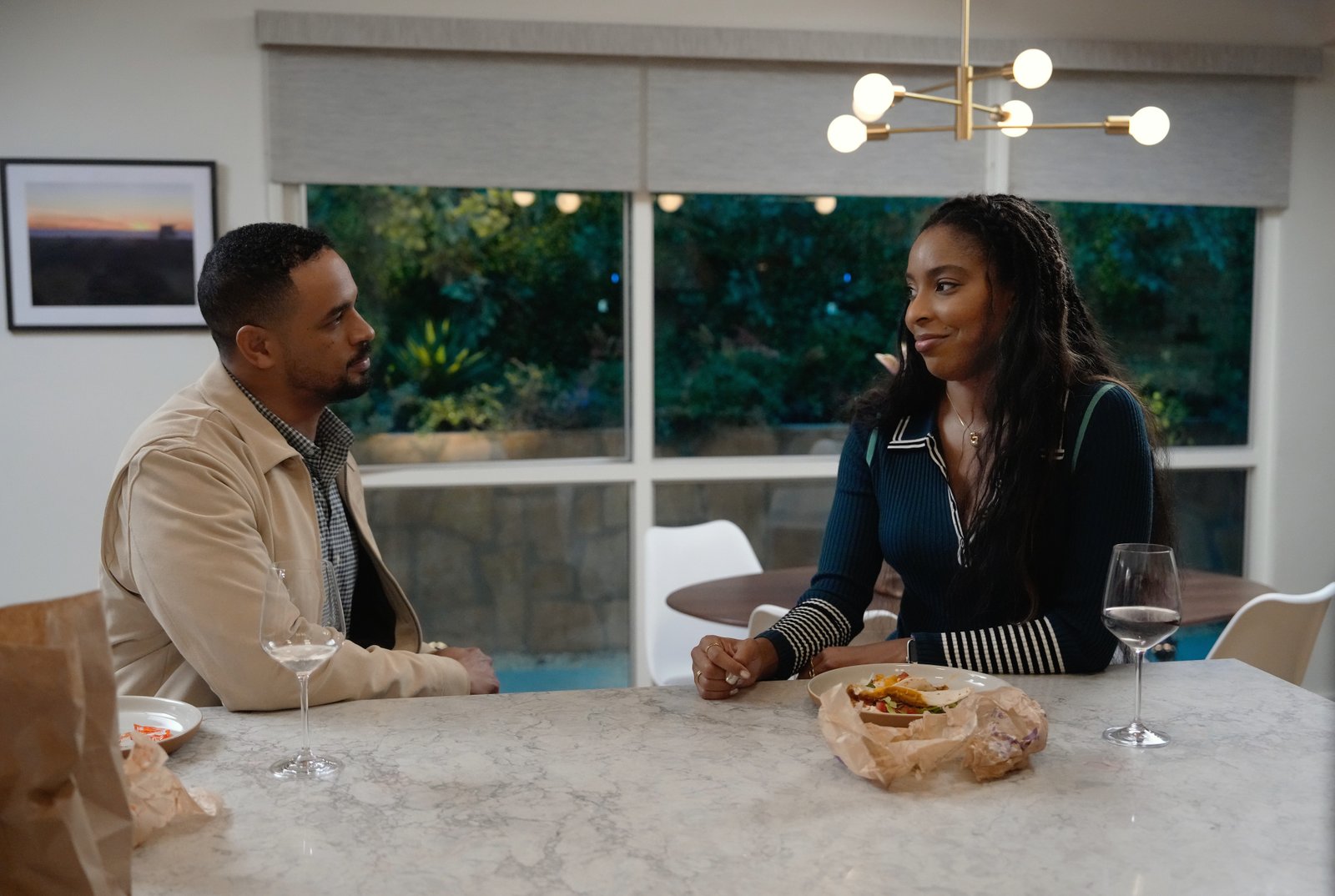 Damon Wayans Jr. as Derrick and Jessica Williams as Gaby, sat at a table facing each other on the same side, in Shrinking Season 3.