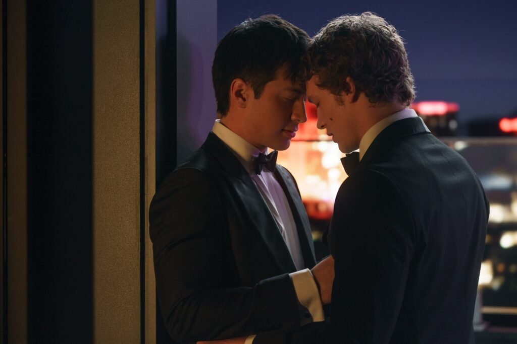 Hudson Williams as Shane Hollander and Connor Storrie as Ilya Rozanov in Heated Rivalry, wearing suits and standing with their foreheads touching in an intimate moment.