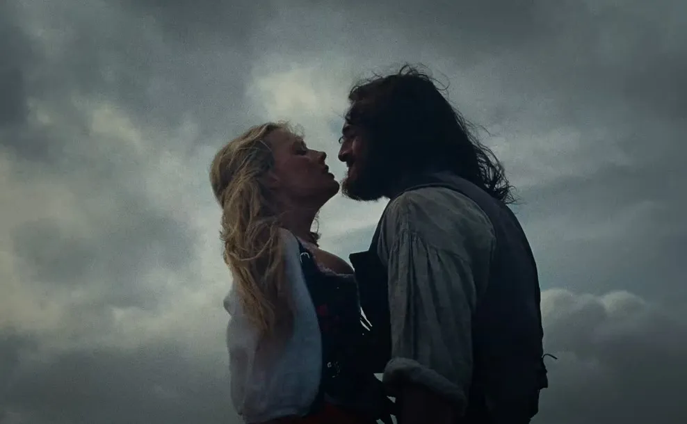 Margot Robbie as Cathy is embraced by Jacob Elordi as Heathcliff underneath a stormy sky in Wuthering Heights