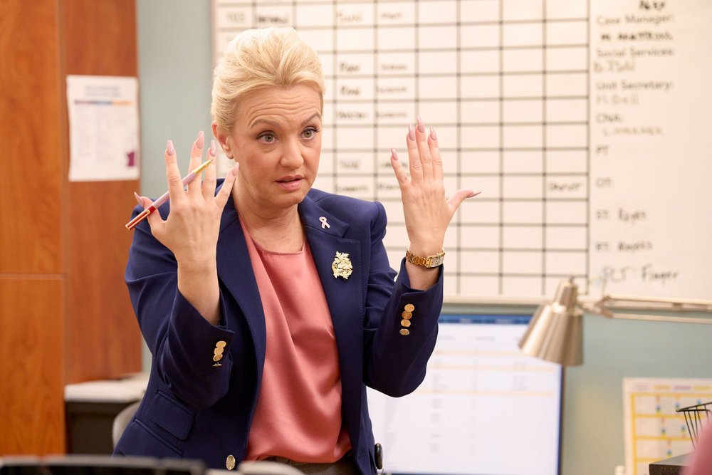 Wendi McLendon-Covey as Joyce with her hands facing forwards in front of her in St. Denis Medical