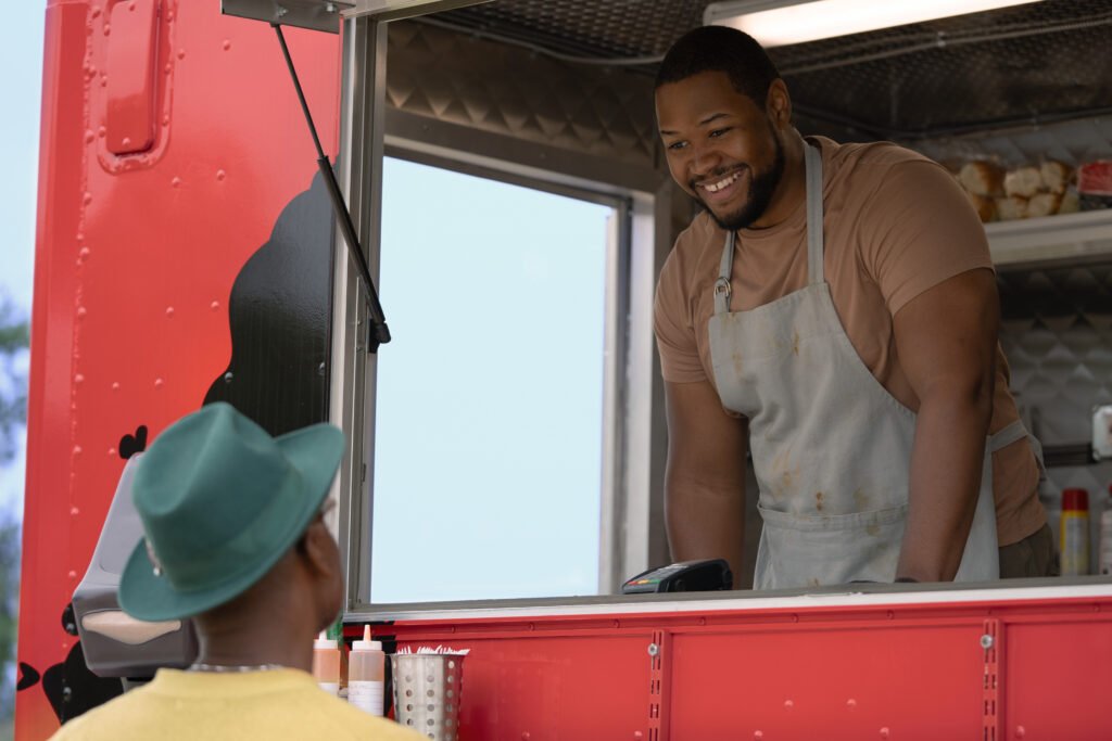 Luke Tennie as Sean stood inside his food truck speaking to a customer in Shrinking Season 3 